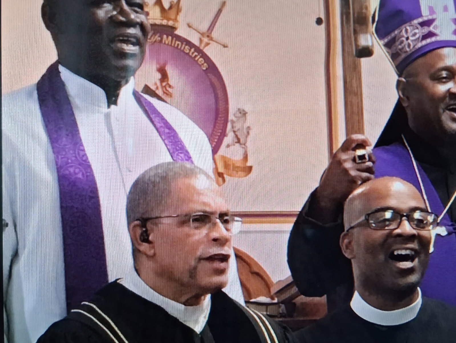 Bishop Maxwell Roberts in a white robe and purple stole, standing with fellow clergy
